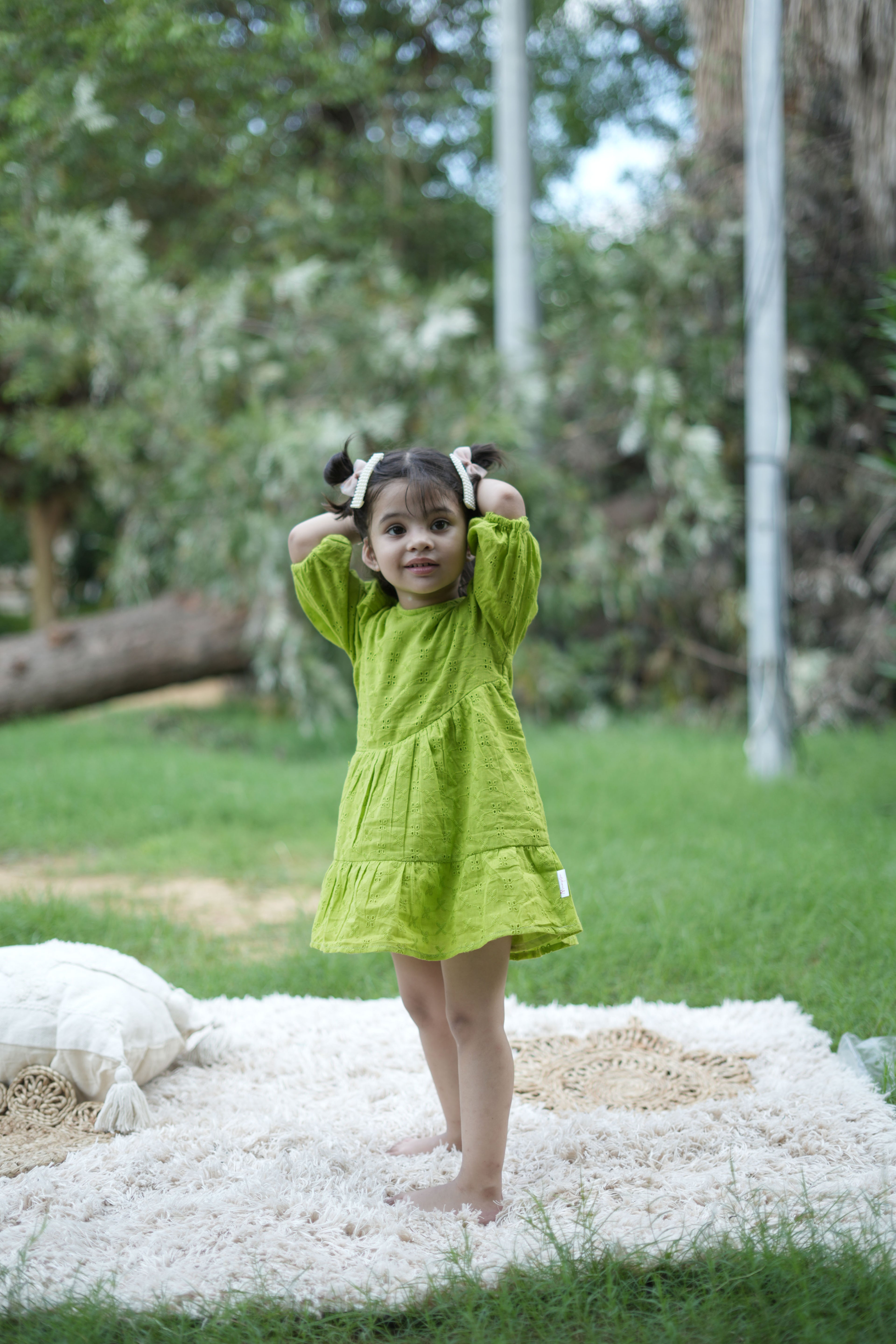 Young girl in a green dress standing on a white blanket outdoors with trees in the background